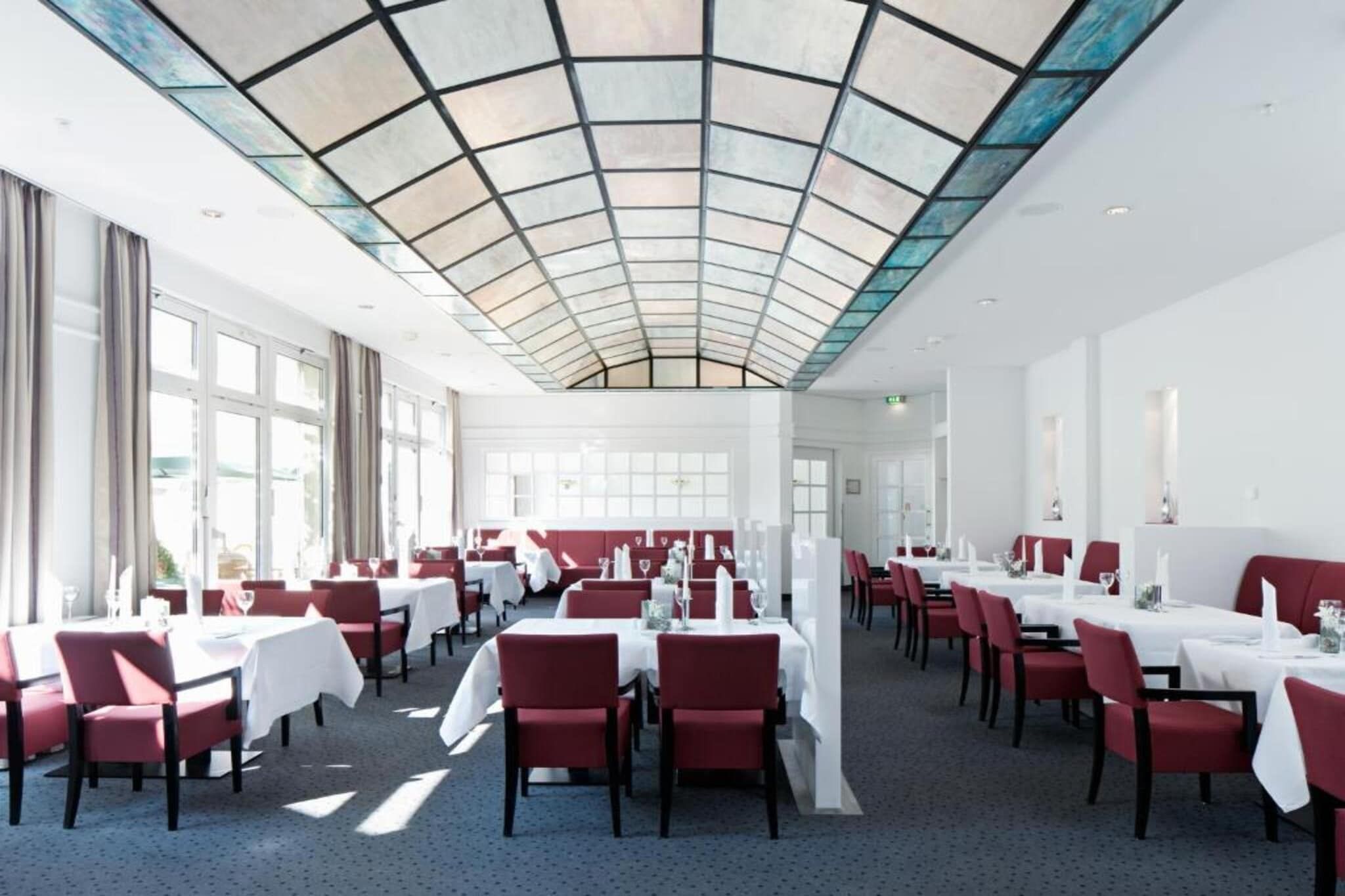 Un vaste espace dédié à la salle à manger, avec des tables et des chaises, un plafond haut agrémenté d’un panneau de verre et de grandes fenêtres laissant entrer la lumière naturelle.