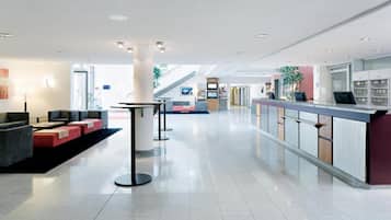 A modern hotel lobby with a reception desk, seating area, and a staircase leading to upper floors.