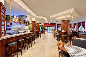 A hotel lobby with a bar area, seating arrangements, and a view of the outside.
