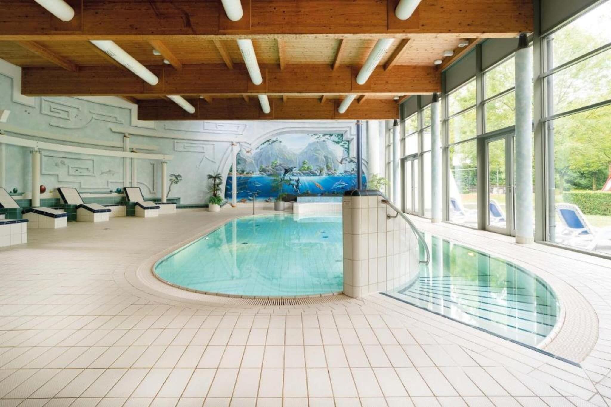 An indoor swimming pool with a view of a mountainous landscape through a large window.
