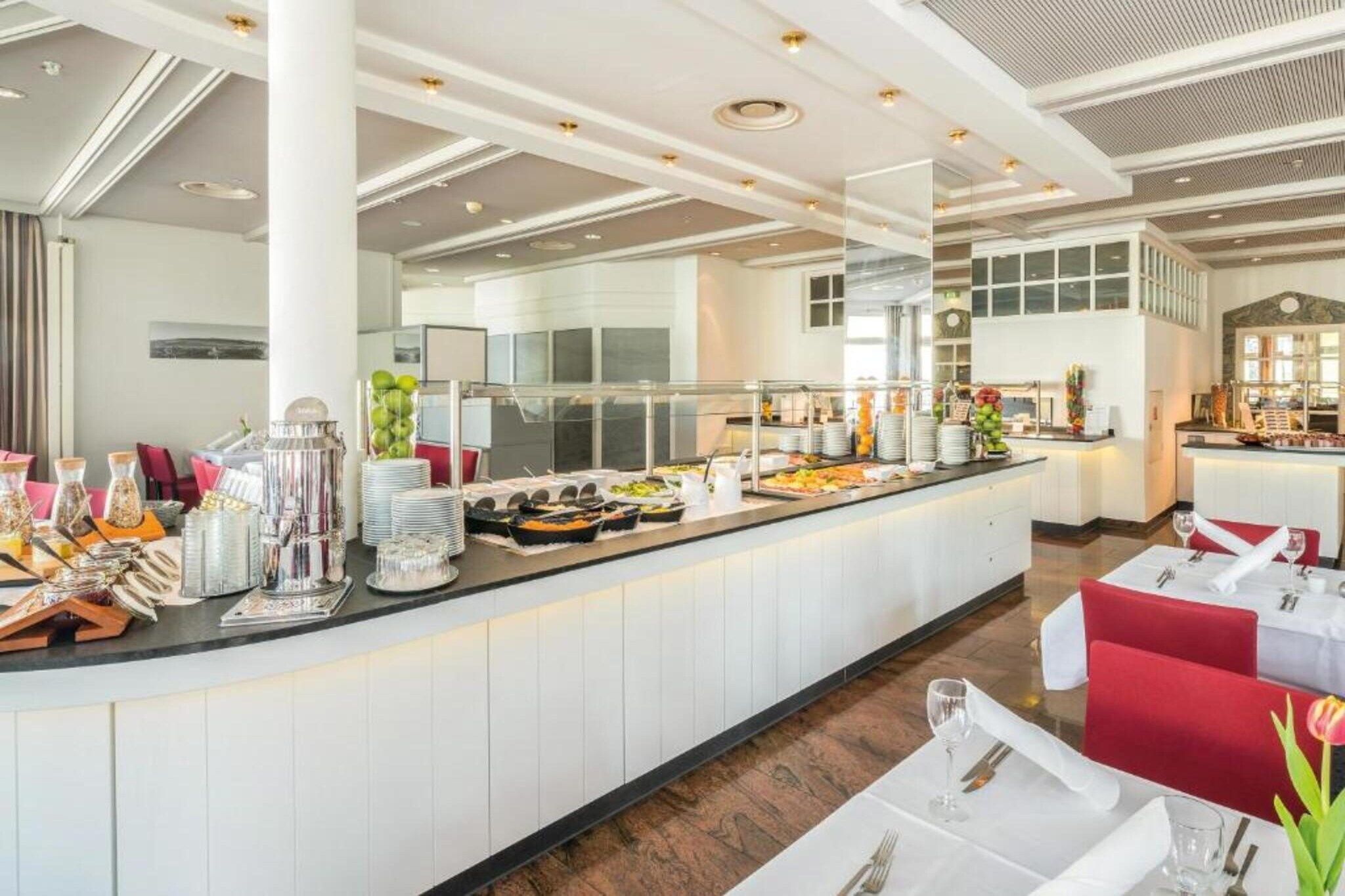 Ein Buffetbereich mit vielfältigen Speisen, ein Sitzbereich mit Tischen und Stühlen sowie ein modernes Decken-Design.