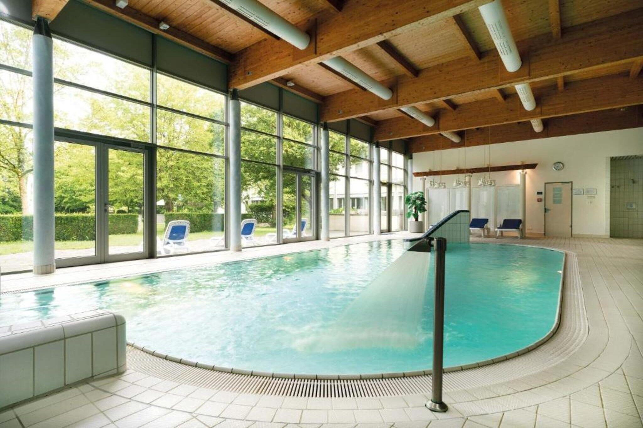Ein Innenpool mit großen Glaswänden, einer Holzbalkendecke und einem gefliesten Boden.