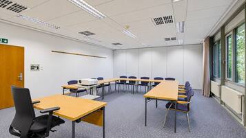 A conference room with a long table, chairs, a projector, and a door with an emergency exit sign.
