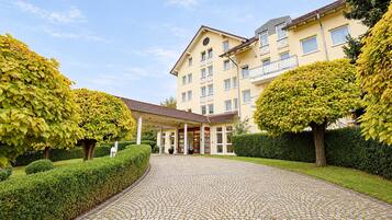 A hotel entrance with a cobblestone pathway leading to a covered area, surrounded by well-maintained hedges and trees.