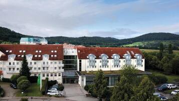 A multi-story hotel with a red-tiled roof, a central courtyard, and a view of surrounding hills.