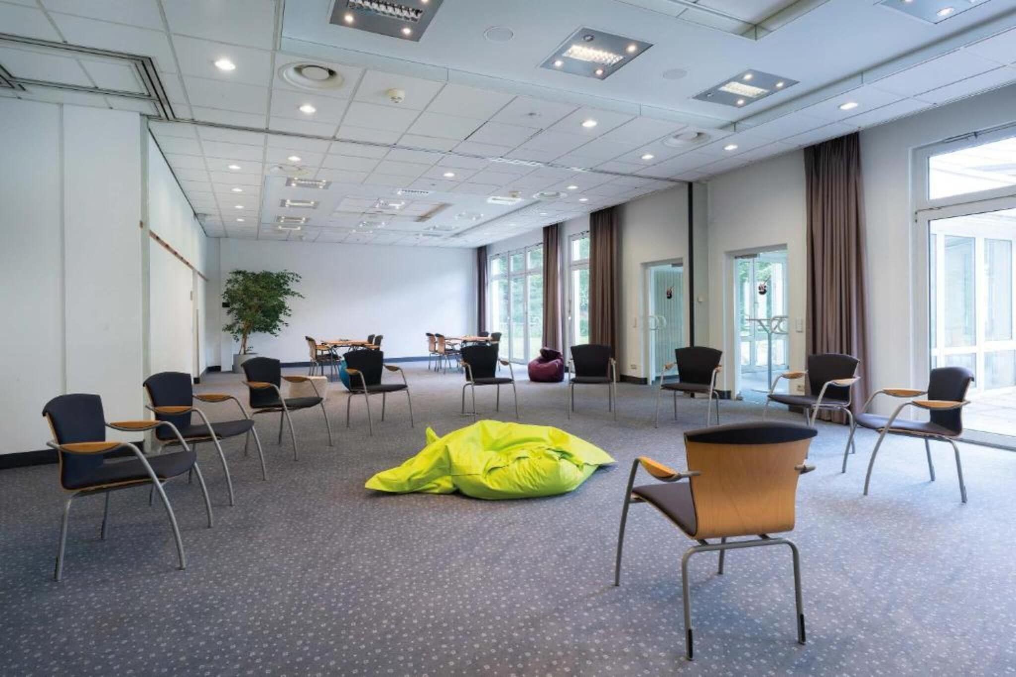 A conference room with multiple chairs, a large window, and a plant.