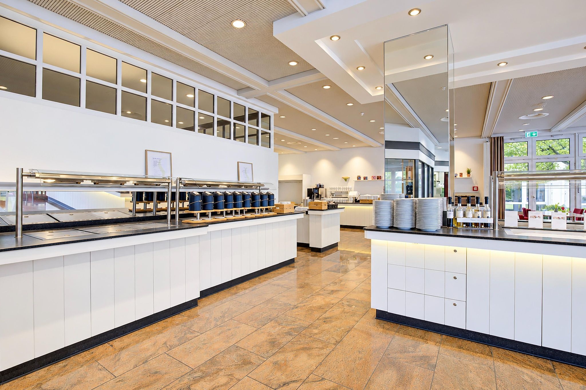 Eine moderne Hotelhalle mit einer Rezeption, einer Kaffeestation und einer Sitzecke mit Tischen und Stühlen.