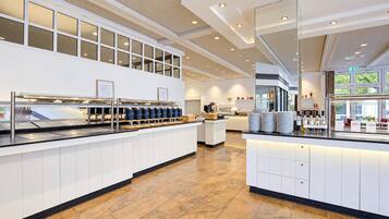 Eine moderne Hotelhalle mit einer Rezeption, einer Kaffeestation und einer Sitzecke mit Tischen und Stühlen.