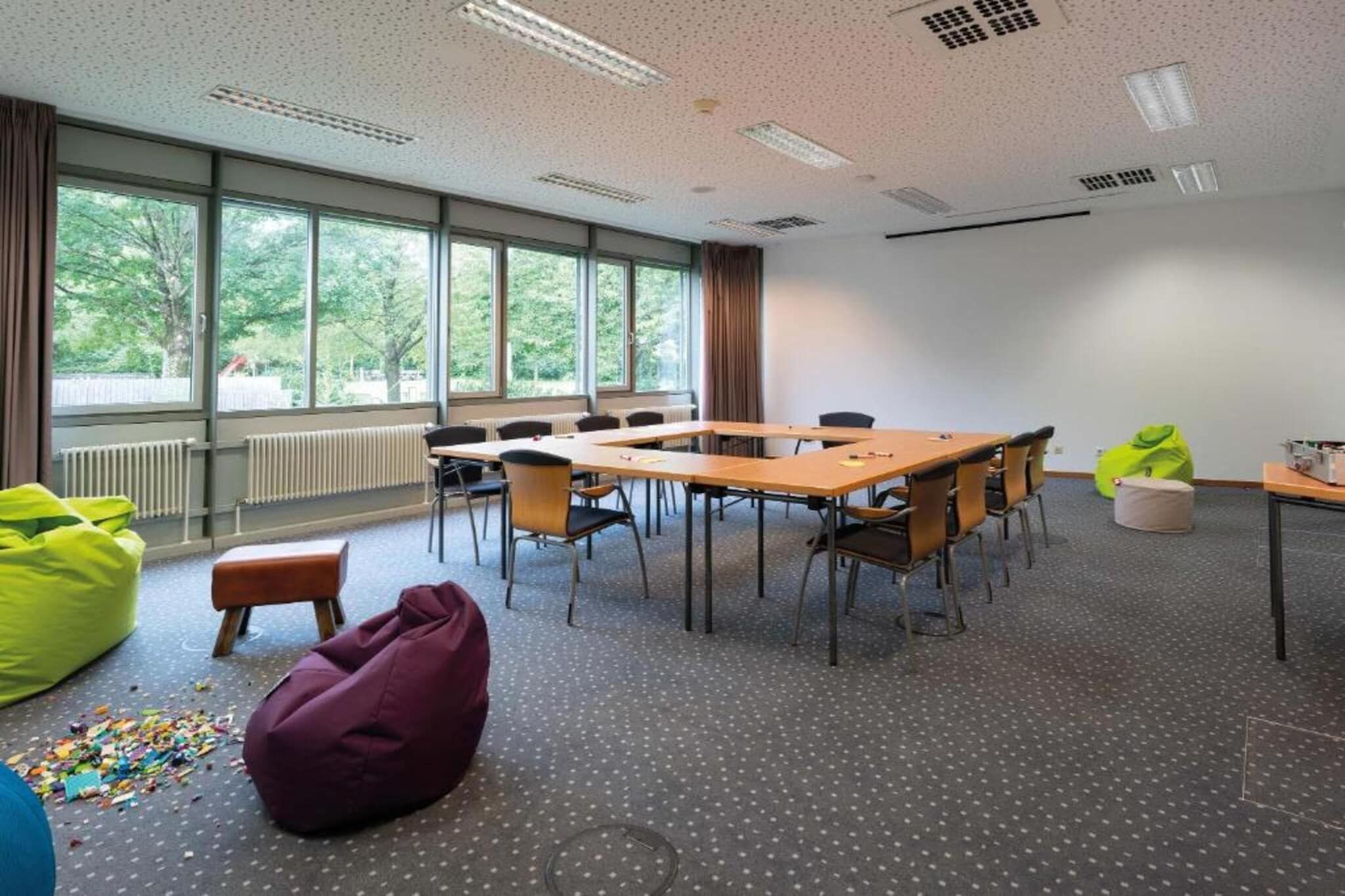 A conference room with a large table, chairs, bean bags, and a view of trees through the windows.