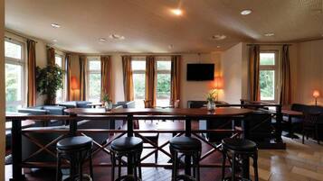 A bar area with a long counter, stools, and a TV mounted on the wall.