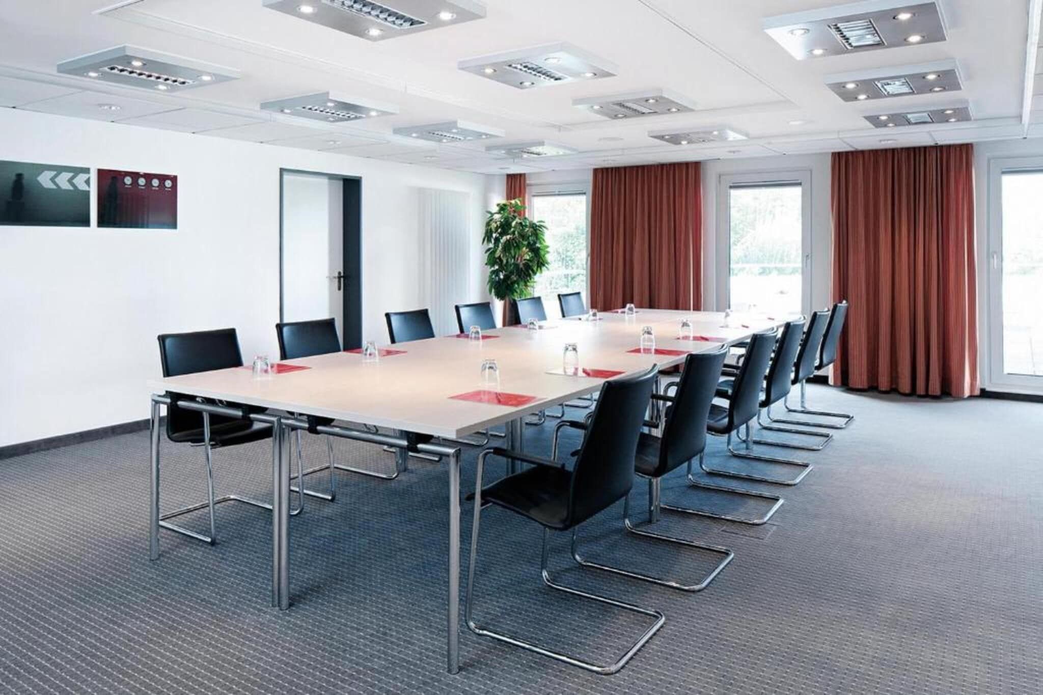 Un salón de conferencias con una mesa larga, sillas y una planta.