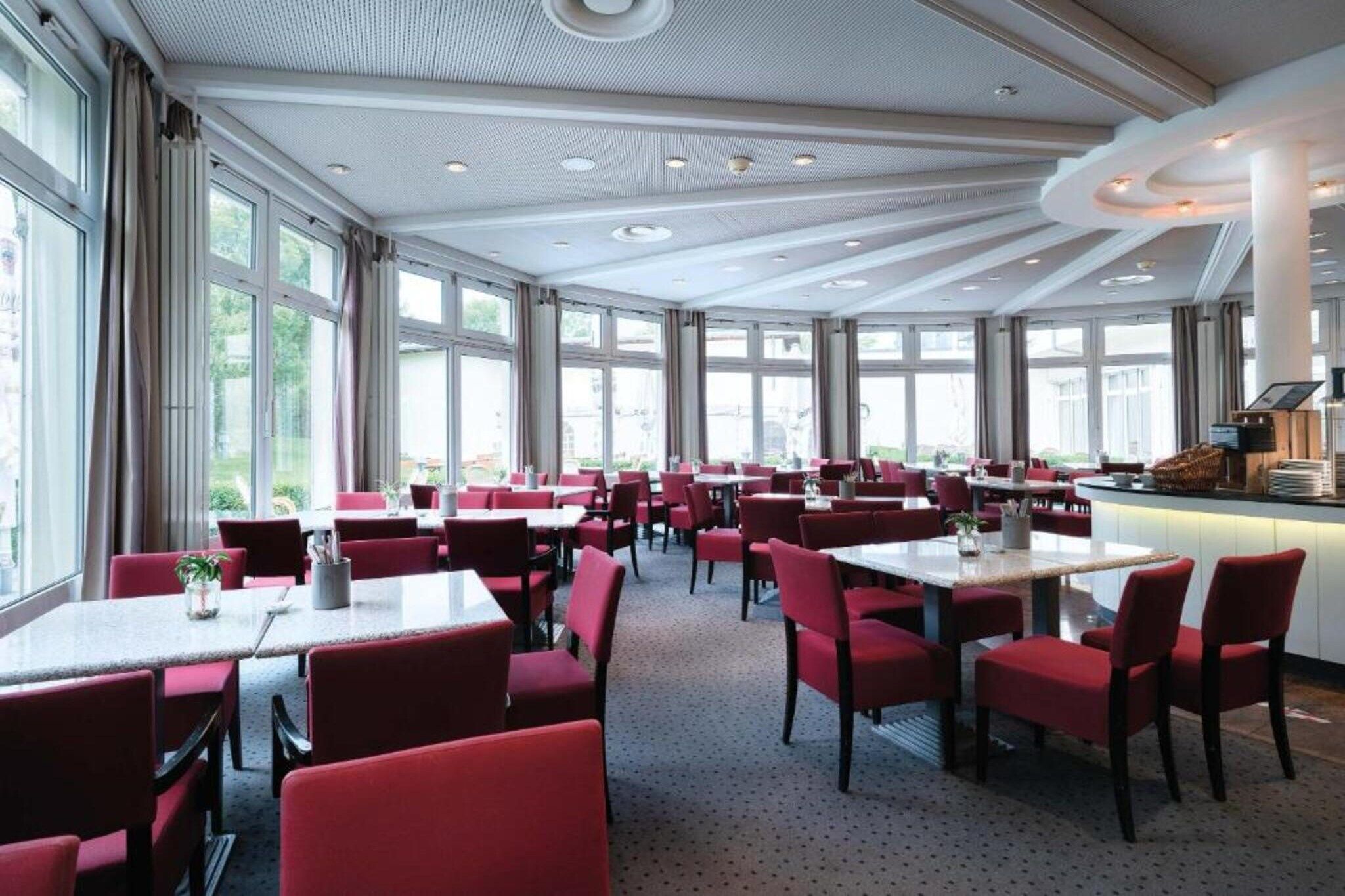 Ein geräumiger Essbereich mit mehreren Tischen und Stühlen, großen Fenstern und einem modernen Deckenstil.