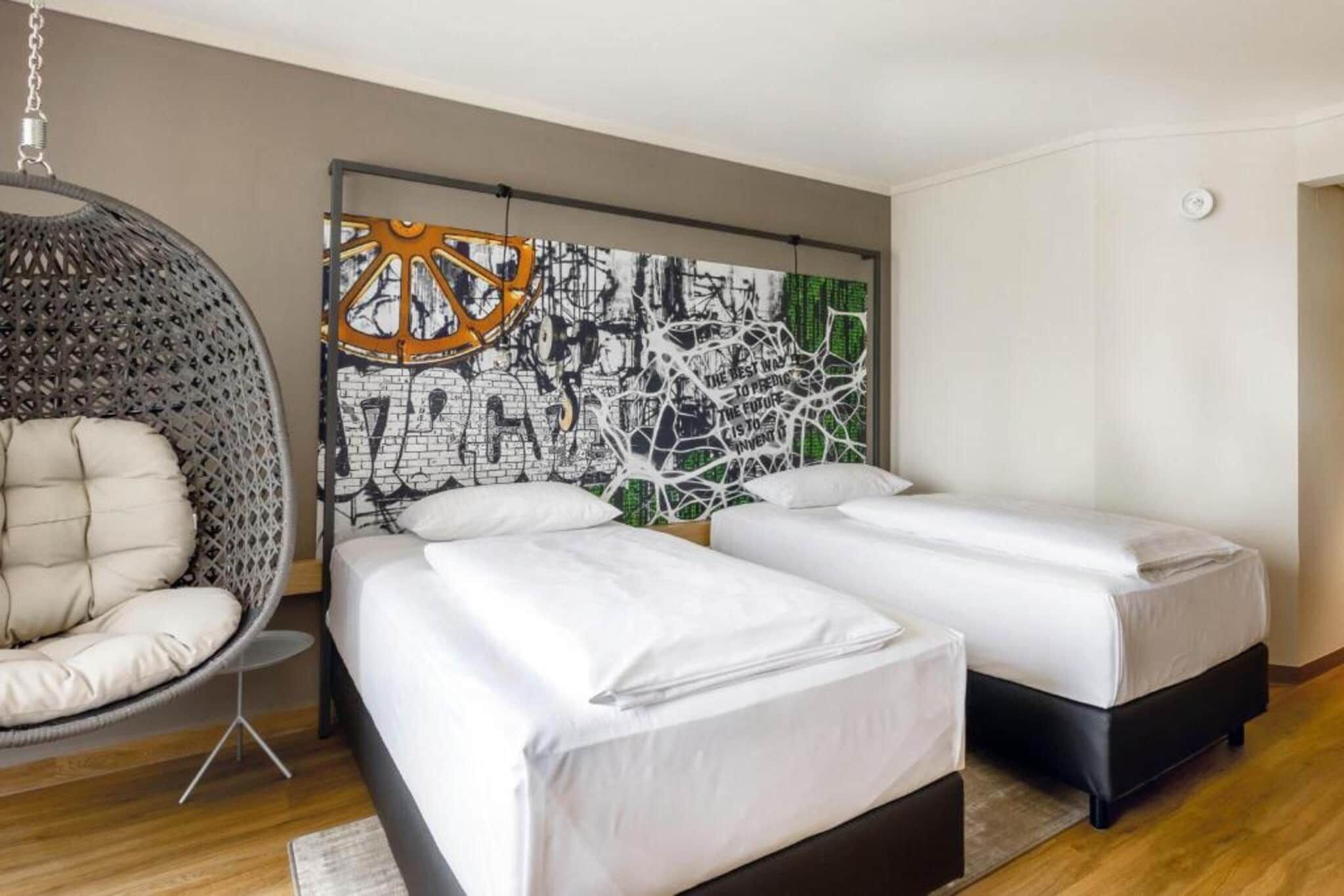 Un dormitorio moderno con dos camas, una silla colgante y una gran obra de arte abstracta en la pared.