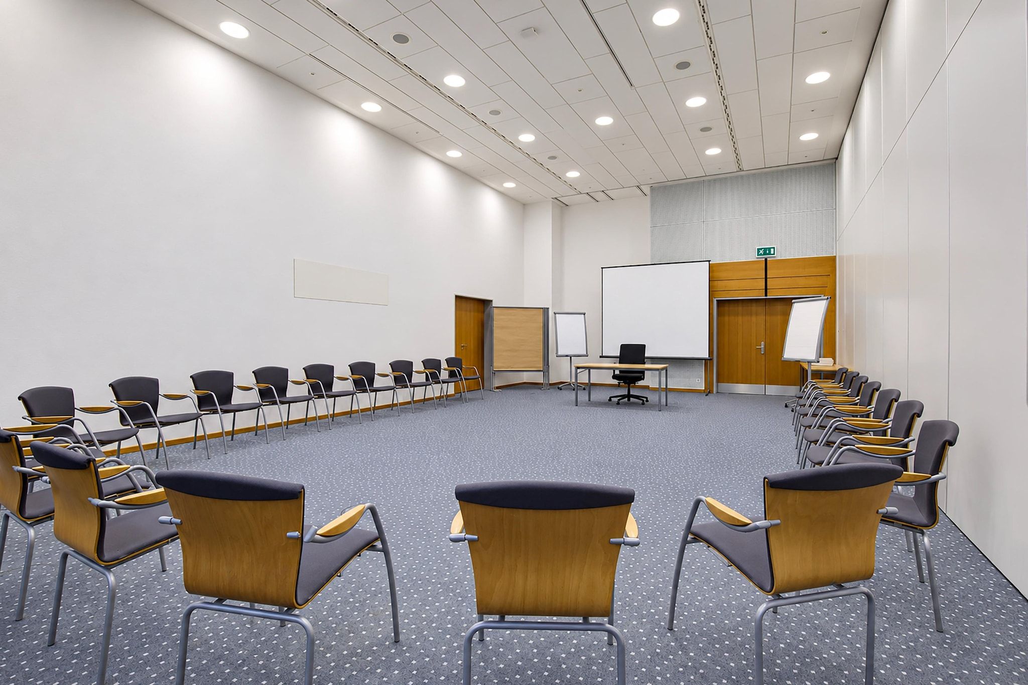 Ein Konferenzraum mit einem langen Tisch, mehreren Stühlen, einer Whiteboard-Tafel und einer Tür mit einem Ausgangsschild.