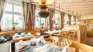 Un ristorante con arredi in legno, tavoli apparecchiati con tovaglioli bianchi e bicchieri, e vista sull'esterno attraverso ampie finestre.