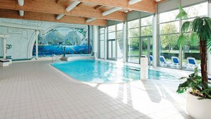 Una piscina interna con un murale, travi a cassetto in legno e vista sull'esterno.