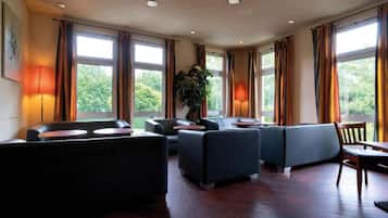 A spacious lounge area with multiple seating options, large windows, and a potted plant.