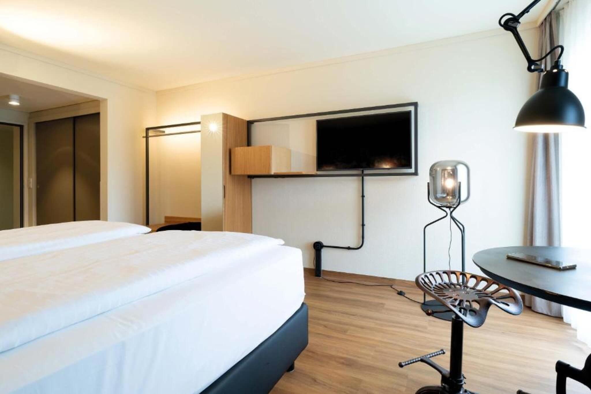 Une chambre d’hôtel équipée d’un lit, d’un bureau, d’une chaise, d’un téléviseur fixé au mur et d’une lampe.