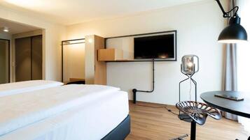 Une chambre d’hôtel équipée d’un lit, d’un bureau, d’une chaise, d’un téléviseur fixé au mur et d’une lampe.
