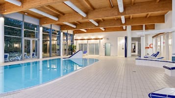 Ein Innenpool mit großen Glaswänden, Fliesenboden und Holzbalkendecke.