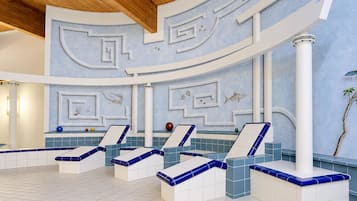 Ein Wellnessbereich mit mehreren Liegestühlen, einem Pool und dekorativen Wandbildern.