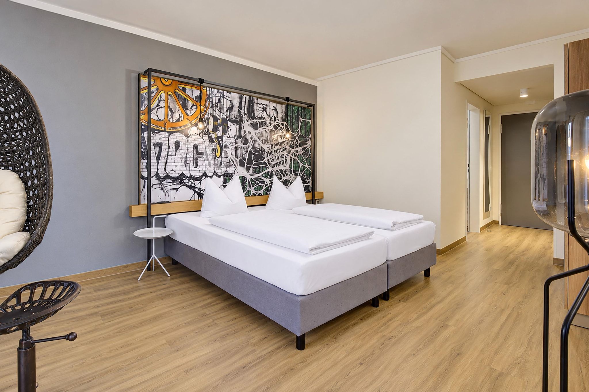 Habitación de hotel moderna con una cama grande, una mesita auxiliar, una silla y una obra de arte en la pared.