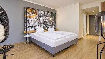 Habitación de hotel moderna con una cama grande, una mesita auxiliar, una silla y una obra de arte en la pared.