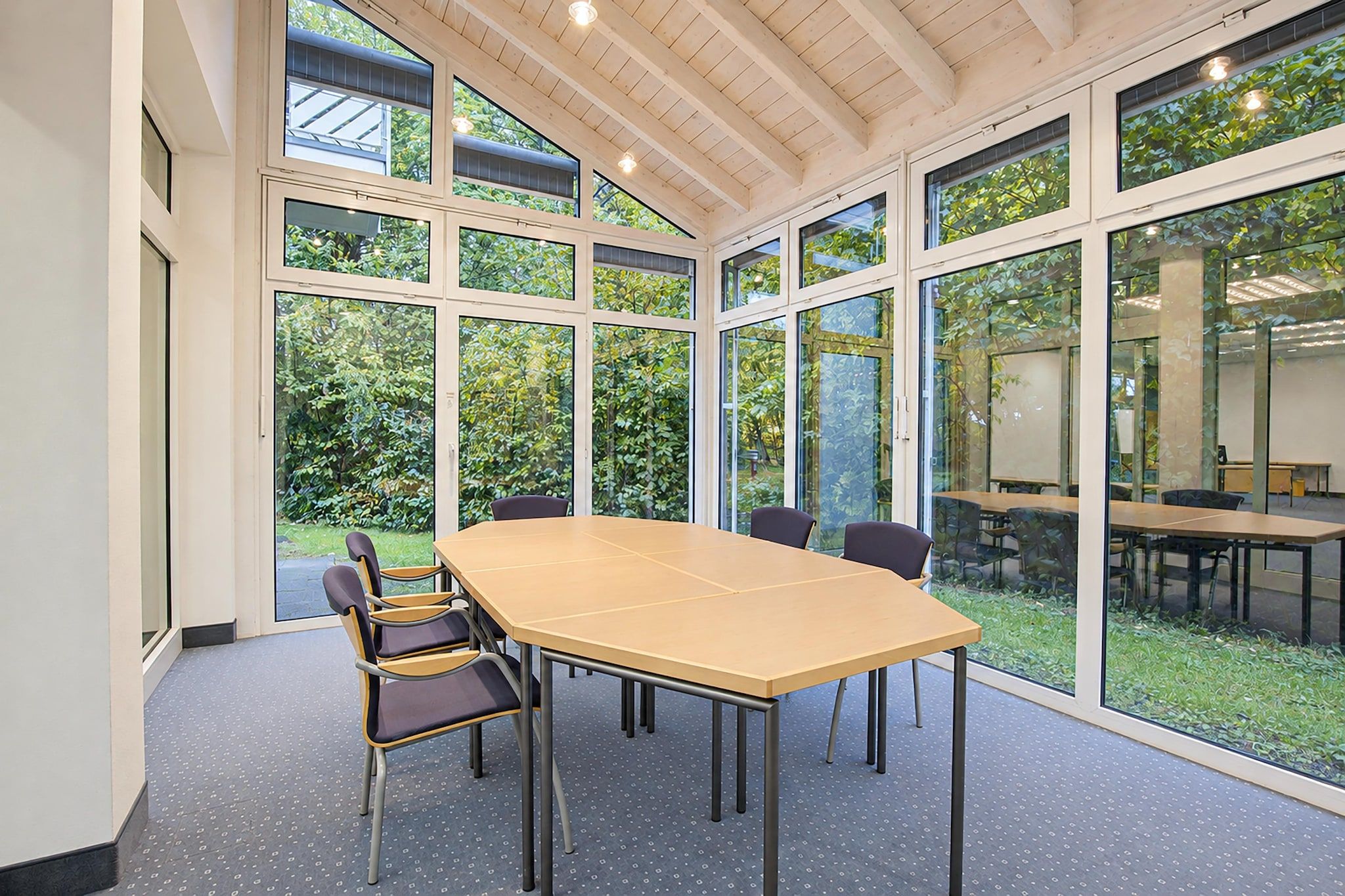 A conference room with a large table and chairs, large windows, and a view of greenery outside.