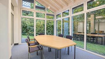 A conference room with a large table and chairs, large windows, and a view of greenery outside.
