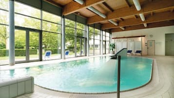 Ein Innenpool mit großen Glaswänden, einer Holzbalkendecke und einem gefliesten Boden.