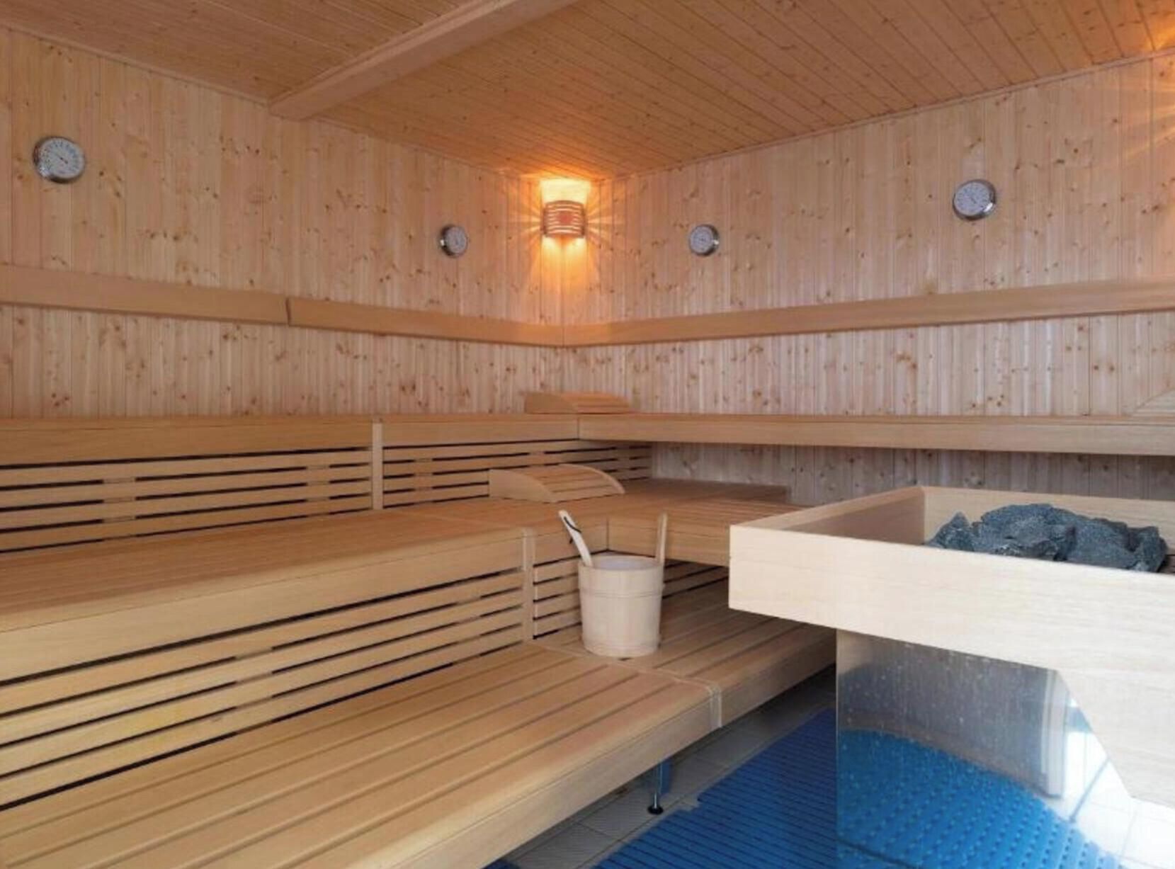 A sauna with wooden benches, a bucket, and a stone basin.