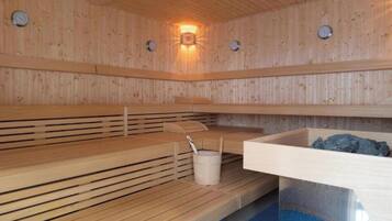 A sauna with wooden benches, a bucket, and a stone basin.