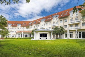 A multi-story building with a red-tiled roof, a central courtyard with a bench, and a grassy area.