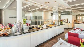 Ein Buffetbereich mit vielfältigen Speisen, ein Sitzbereich mit Tischen und Stühlen sowie ein modernes Decken-Design.
