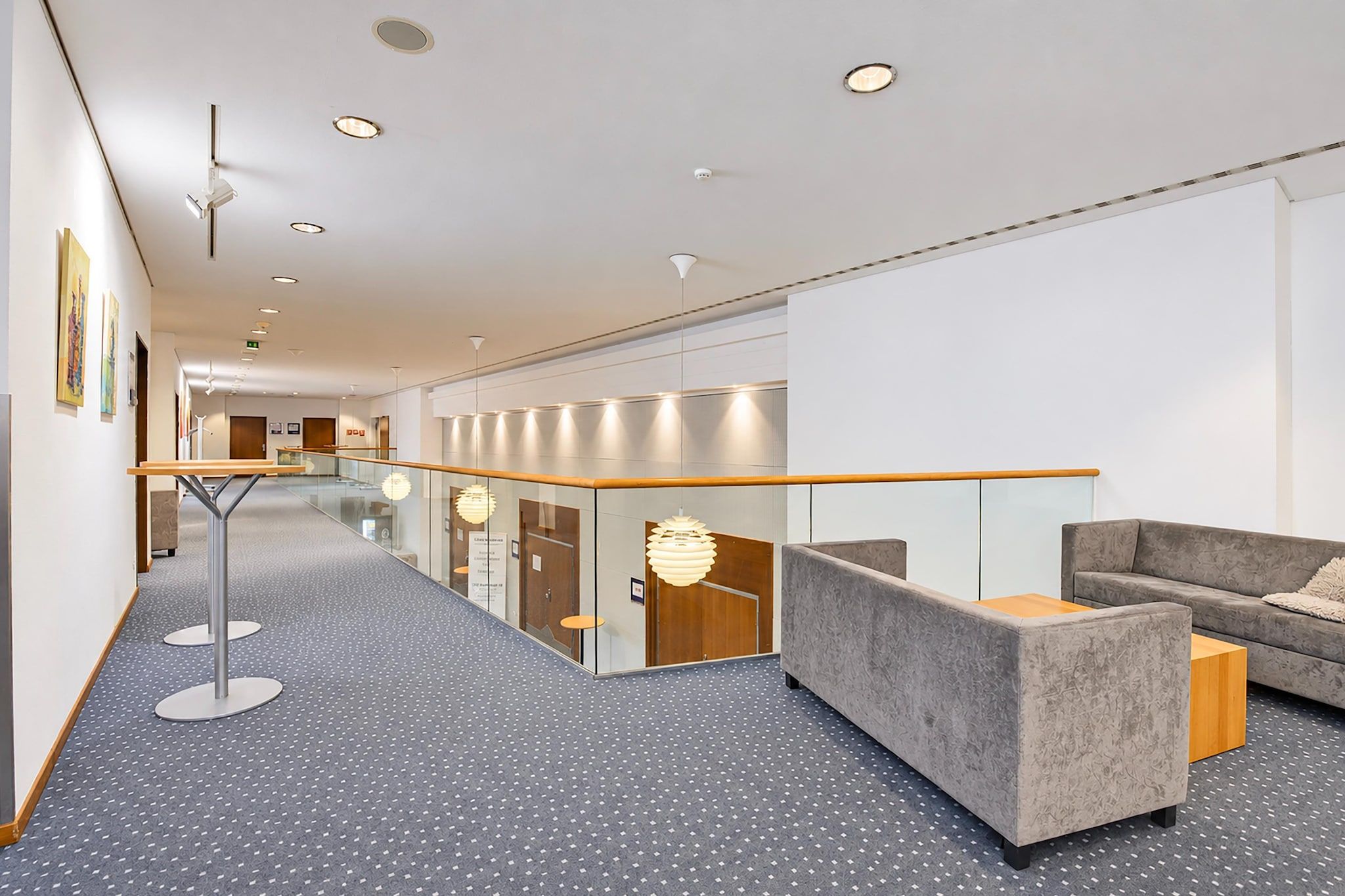 Eine moderne Hotelhalle mit Glastrennwand, einer Sitzecke inklusive Sofa und Sesseln, und einem gestreiften Boden.