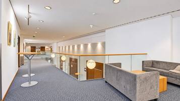 Eine moderne Hotelhalle mit Glastrennwand, einer Sitzecke inklusive Sofa und Sesseln, und einem gestreiften Boden.