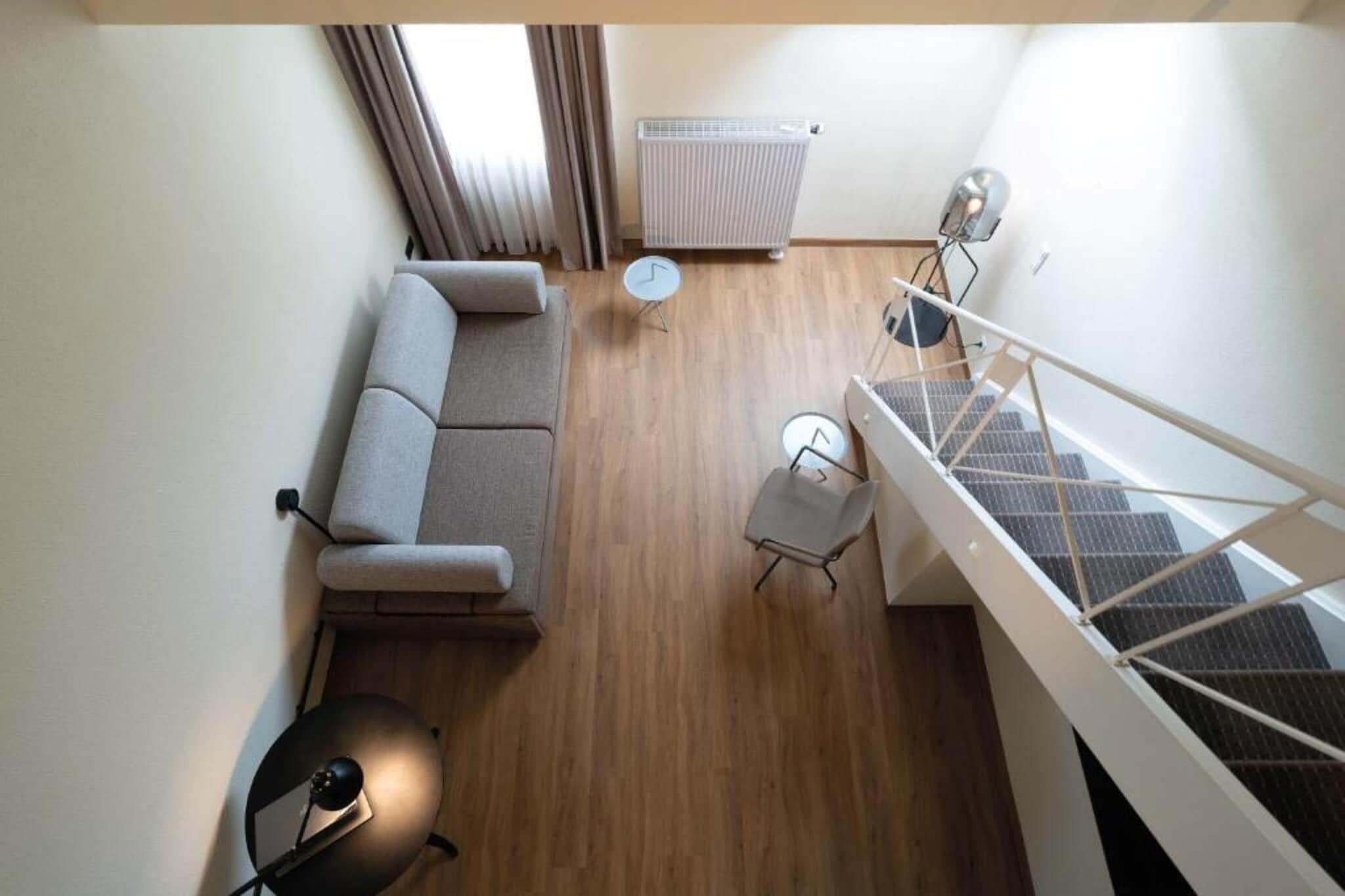 Un appartement moderne comprenant un canapé, une petite table ronde, une chaise, un radiateur et un escalier.