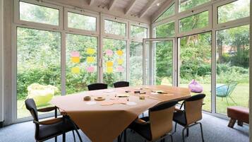 Ein Konferenzraum mit großem Tisch, Stühlen und Blick auf Grün durch große Fenster.