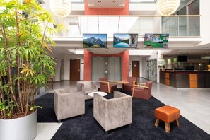 Un hall d’entrée moderne avec des sièges, une grande plante en pot et un coin cuisine à l’arrière-plan.