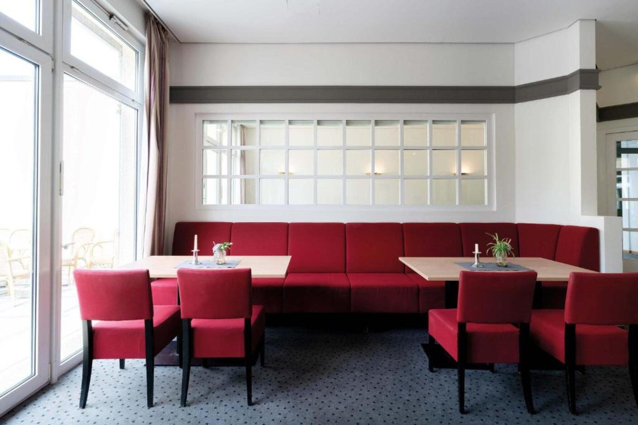 A dining area with a red booth seating arrangement, a long table, and chairs.