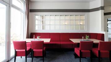 A dining area with a red booth seating arrangement, a long table, and chairs.
