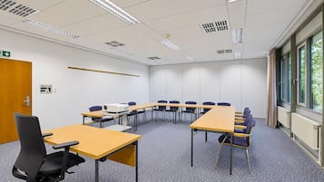 Un salón de conferencias con una larga mesa, sillas, un proyector y una puerta con letrero de salida de emergencia.