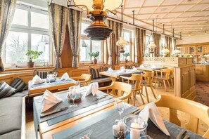 A restaurant with wooden furniture, tables set with white napkins and glasses, and a view of the outdoors through large windows. - Hotel Bad Boll-Apartment (Bad Boll)