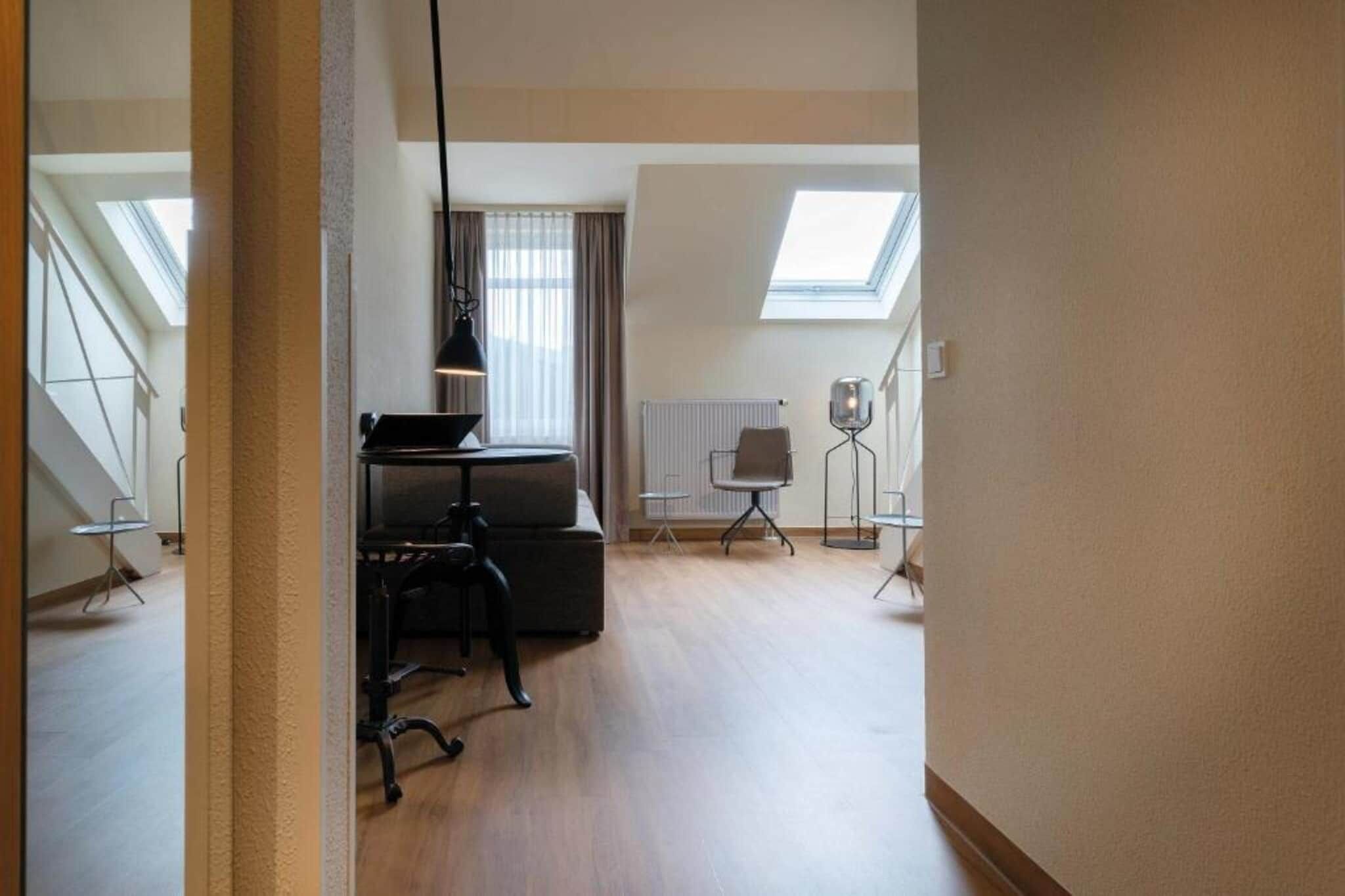 Een ruime kamer met een hoge plafond, een dakraam, een bureau met stoel en een radiator.