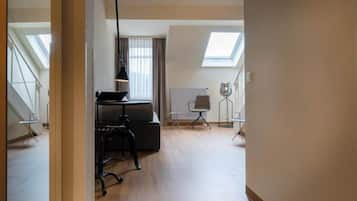 Een ruime kamer met een hoge plafond, een dakraam, een bureau met stoel en een radiator.