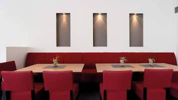Un área de comedor con un sofá rojo largo, una mesa rectangular y sillas rojas. Hay tres lámparas fijadas a la pared sobre la mesa.