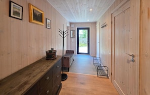A wooden interior hallway with a bench, a coat rack, and a door leading outside.
