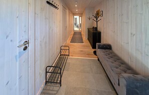 A hallway with a wooden floor, a metal rack, a grey sofa, and a door with a handle.