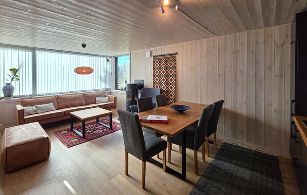 A modern living room with a wooden ceiling, a sofa, a coffee table, and a dining area with chairs and a table.