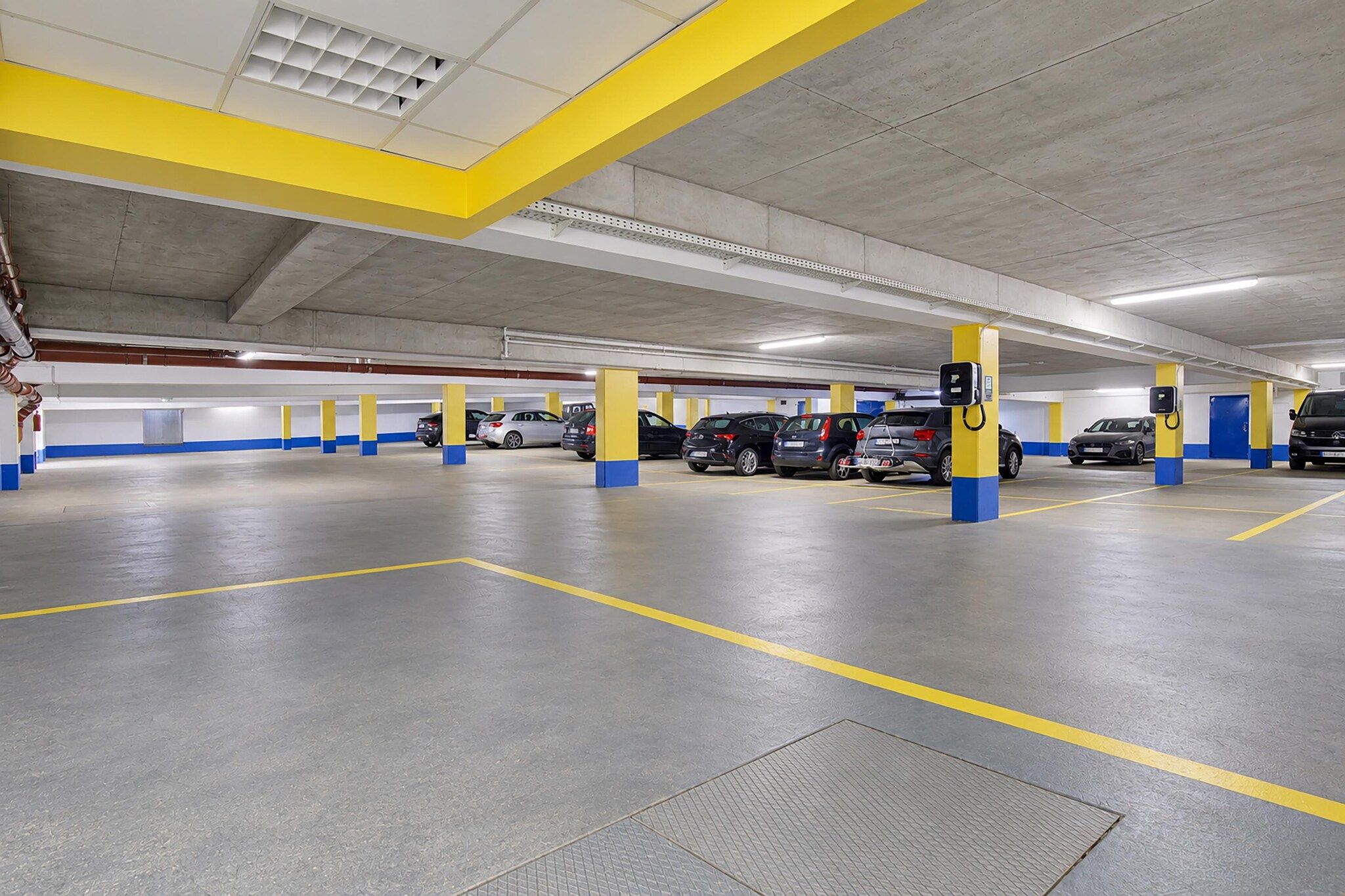 A multi-level parking garage with yellow and blue pillars, electric vehicle charging stations, and a clean, well-lit environment.